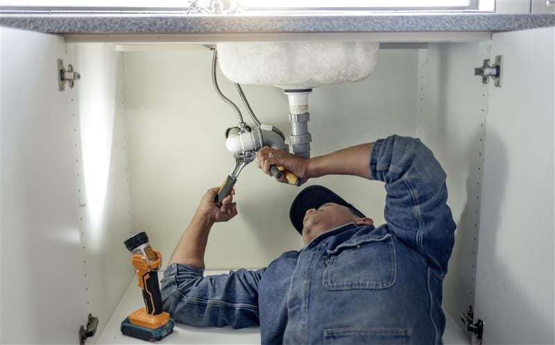 Plumber repairing pipes beneath a bathroom sink in Plantation