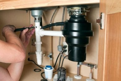 Plumber repairing a garbage disposal beneath a kitchen sink in Plantation