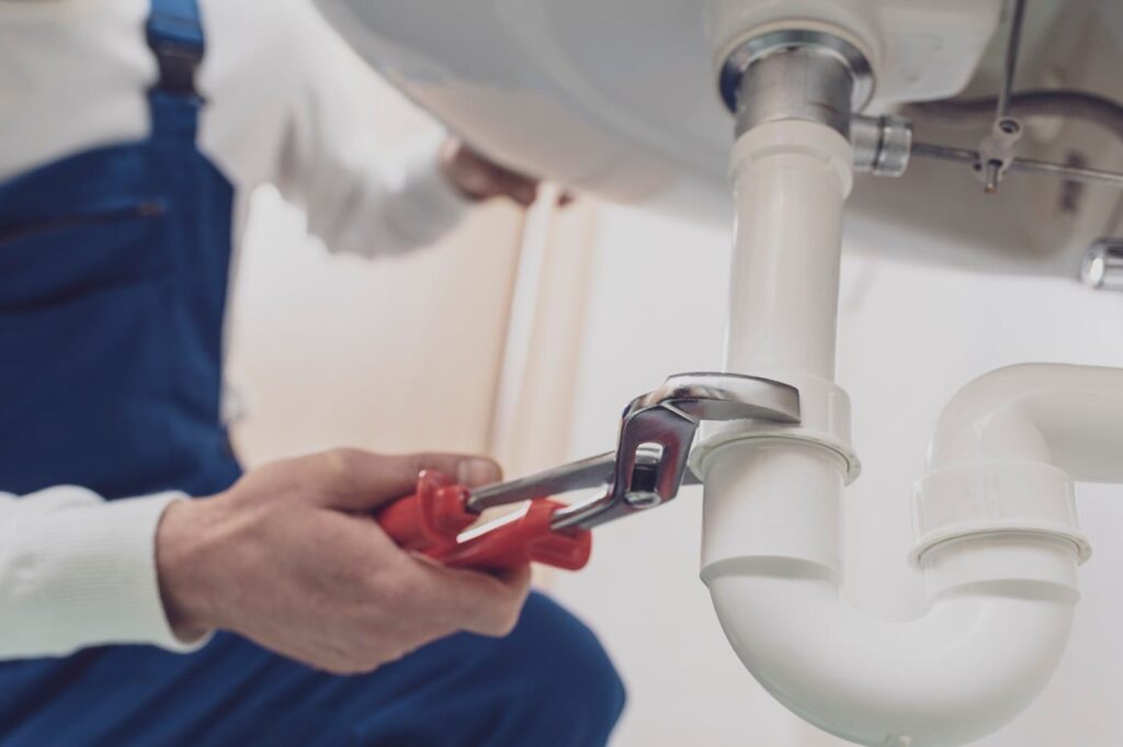 Plumber repairing a white drain pipe beneath a sink in Plantation
