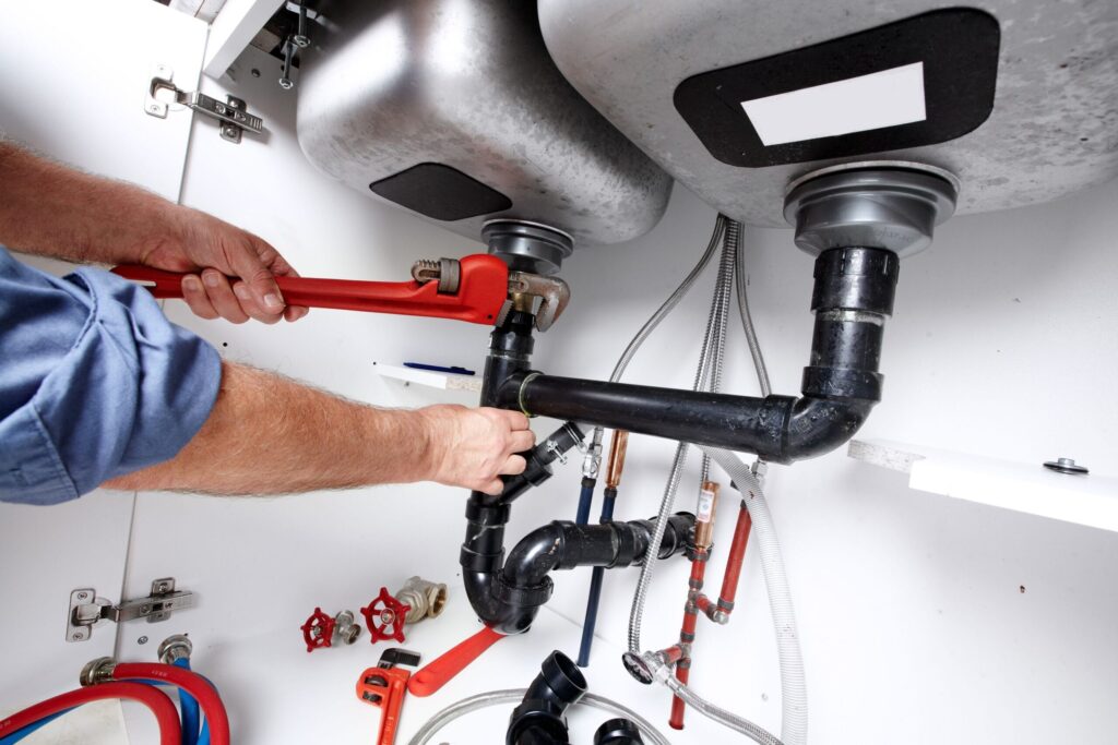 Plumber repairing drain pipes beneath a kitchen sink in Plantation